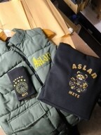 Geschenk Set Grüne Weste und schwarze Sweatshirt mit gelbem ASLAN-Logo und Schrift.